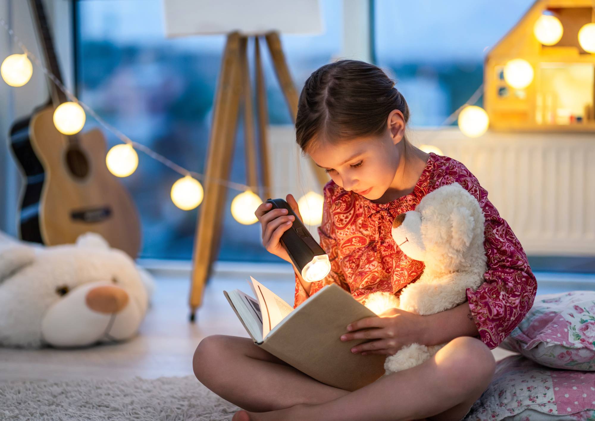Dítě čtoucí knihu při zapnuté lampičce v pokoji