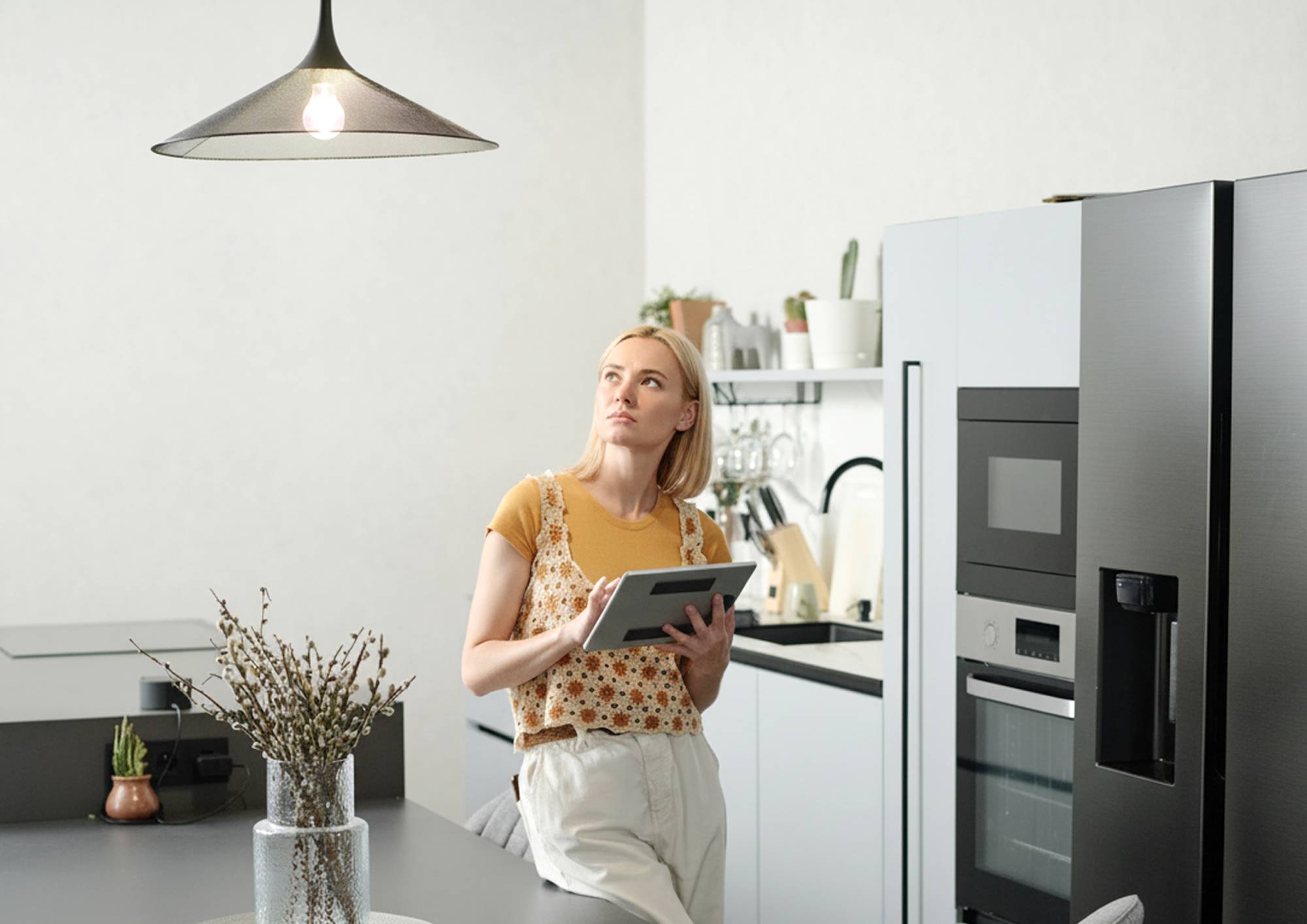 Žena stojící v kuchyni při zapnutém závěsném svítidle