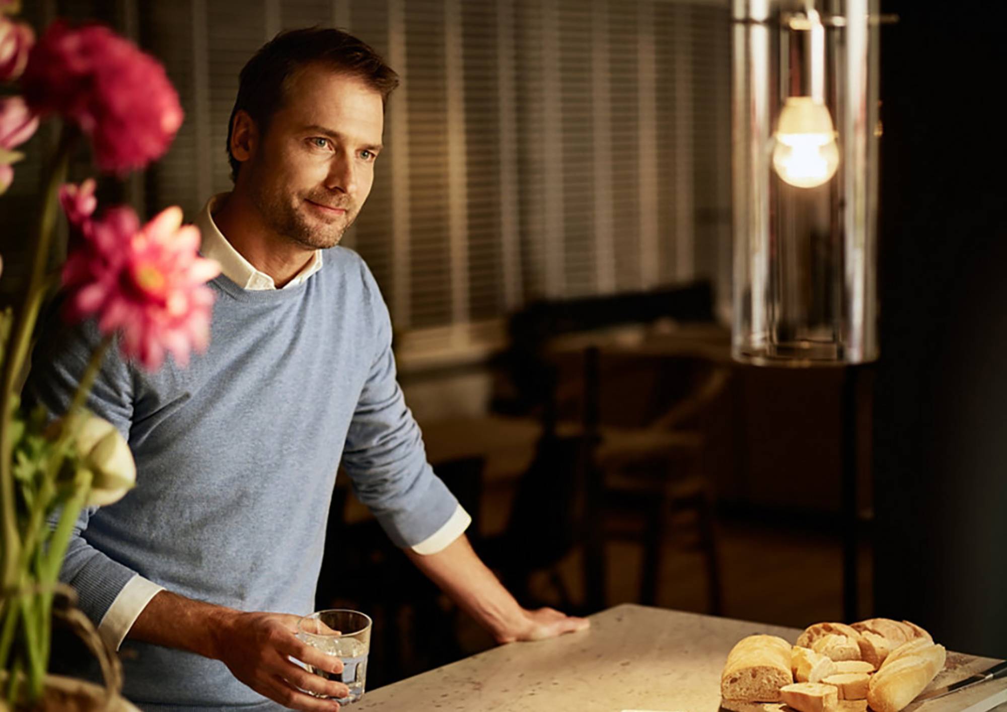 Muž stojící u kuchyňské pracovní desky při zapnutém závěsném svítidle