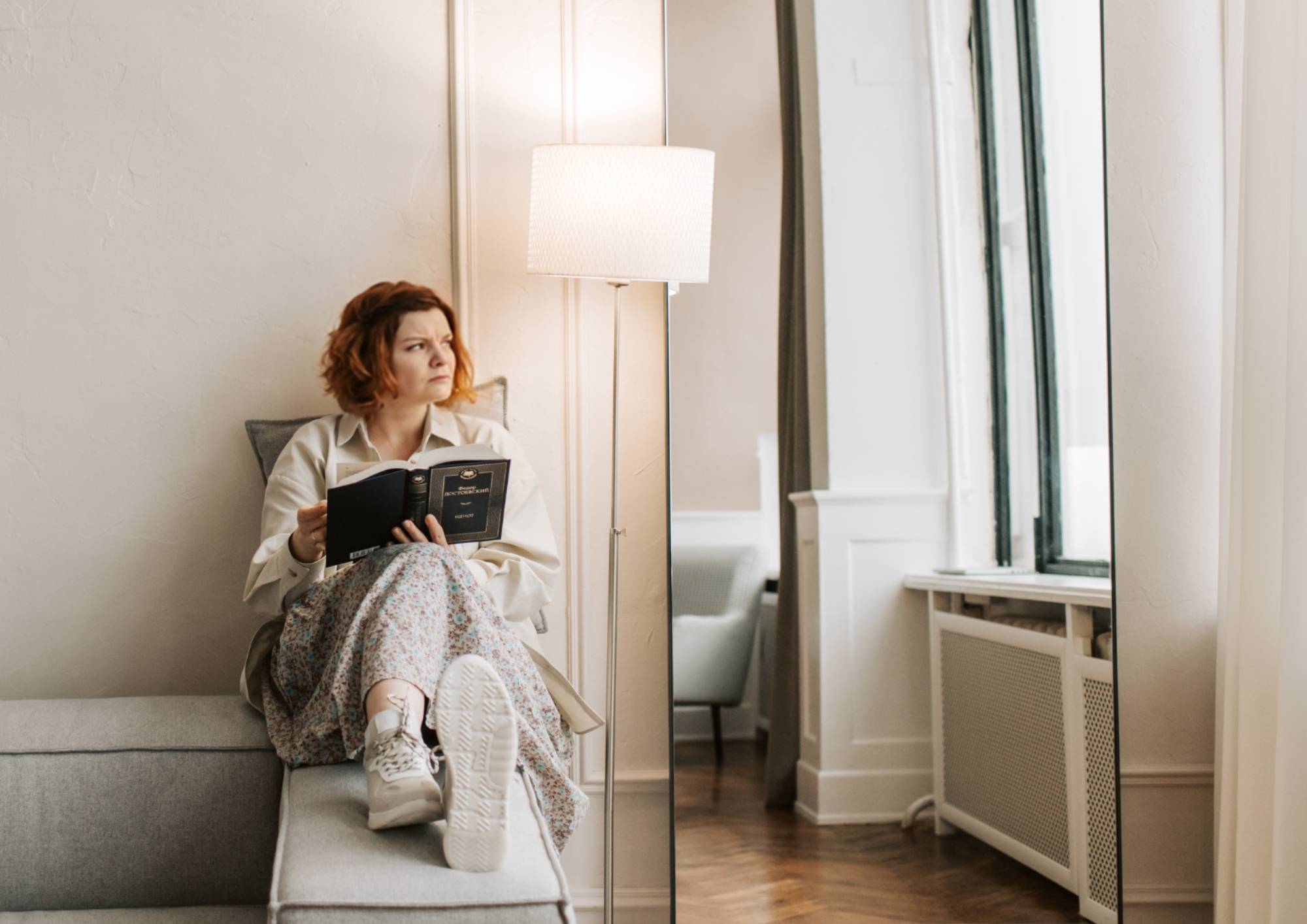 Žena sedící na pohovce při zapnuté stojací lampě v obývacím pokoji